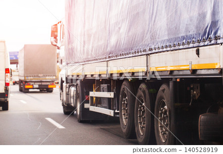 Side view of several heavy goods vehicles on highway during day, large cargo trucks driving on road, transport and logistics concept 140528919
