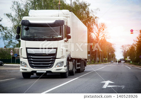 White semi-truck with cargo trailer travels on asphalt road. Long haul vehicle transportation of goods. Logistics supply chain service. 140528926