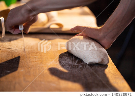 Skilled hands of baker carefully shaping fresh dough loaf on wooden surface dusted with flour preparation for baking bread Skilled hands of baker carefully shaping fresh dough loaf on wooden surface dusted with flour preparation for baking bread 140528971