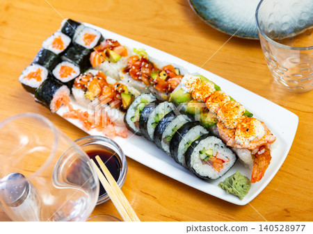 Assorted different types of maki, uramaki, with salmon, served with bowl of soy sauce on plate in restaurant Assorted different types of maki, uramaki, with salmon, served with bowl of soy sauce on plate in restaurant 140528977