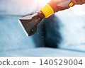 Hand holding cleaning nozzle of wet vacuum cleaner spraying water for deep cleaning upholstery furniture indoors day time professional service 140529004