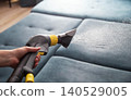 Close-up of hand holding upholstery cleaning tool spraying fine mist onto blue fabric sofa during deep cleaning process in modern home environment 140529005