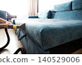 Person hands cleaning sofa upholstery with professional wet vacuum cleaner. Deep cleaning fabric surface of teal sectional couch using water extraction machine indoors 140529006
