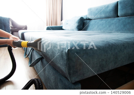 Person hands cleaning sofa upholstery with professional wet vacuum cleaner. Deep cleaning fabric surface of teal sectional couch using water extraction machine indoors Person hands cleaning sofa upholstery with professional wet vacuum cleaner. Deep cleaning fabric surface of teal sectional couch using water extraction machine indoors 140529006