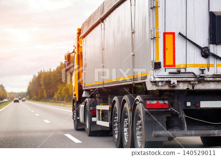 Large semi truck trailer transportation on asphalt highway road at sunset sky driving cargo delivery logistics freight industry commercial vehicle moving goods Large semi truck trailer transportation on asphalt highway road at sunset sky driving cargo delivery logistics freight industry commercial vehicle moving goods 140529011