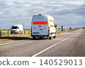 White delivery van traveling highway on cloudy day, rear view of cargo transport vehicle with orange stripe on back doors, journey on asphalt road with power lines in background 140529013