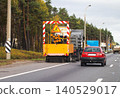 Rear view of yellow road maintenance truck with chevron warning panel and rotating brushes on asphalt highway, red passenger car follows. 140529017