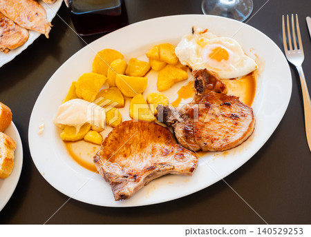 Fried pork with potatoes and fried eggs on plate 140529253