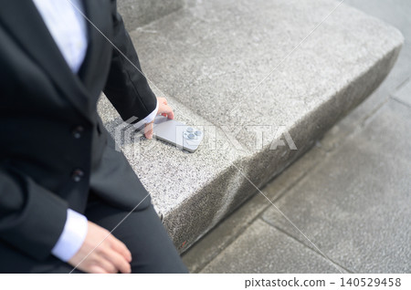 A business scene where someone picks up their smartphone from a bench. 140529458