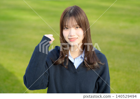 Japanese high school girl makes a victory pose in front of the grass. Japanese high school girl makes a victory pose in front of the grass. 140529494