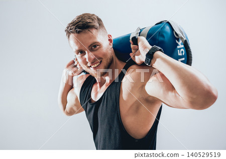 Athletic young man training with sandbags at gray background. Crossfit center 140529519