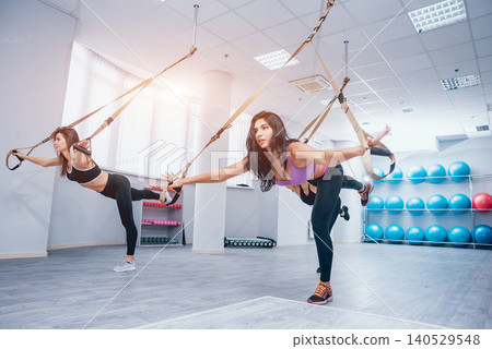 Beautiful young sports women are working out with TRX in gym 140529548
