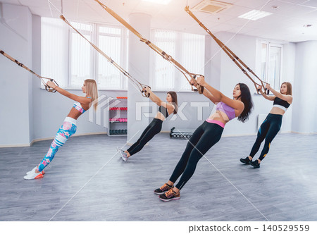 Beautiful young sports women are working out with TRX in gym Beautiful young sports women are working out with TRX in gym 140529559