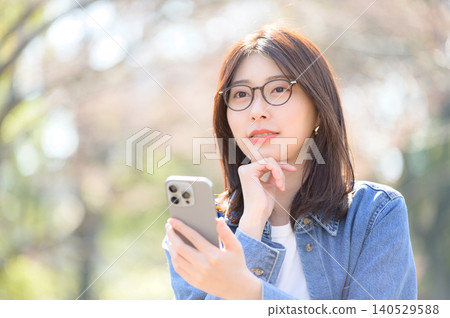 Japanese woman using her smartphone in a park 140529588