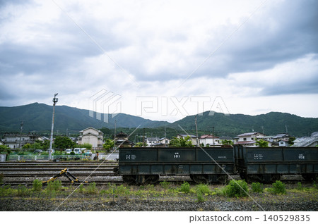 A black open freight car stands on the tracks of a local railway against a backdrop of cloudy skies and mountain ranges. A black open freight car stands on the tracks of a local railway against a backdrop of cloudy skies and mountain ranges. 140529835
