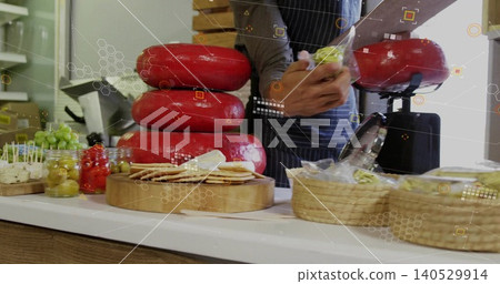 Vendor wearing striped apron wrapping green-wrapped wedge at cheese counter, showing red wax wheels Vendor wearing striped apron wrapping green-wrapped wedge at cheese counter, showing red wax wheels 140529914