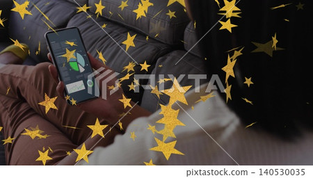 Holding phone, seated woman viewing charts on dark-gray sofa in white-ribbed-top, gold stars Holding phone, seated woman viewing charts on dark-gray sofa in white-ribbed-top, gold stars 140530035