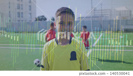 Smiling child in yellow soccer jersey standing on urban field, showing soccer ball, goal overlay 140530041