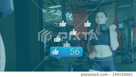 Holding hex dumbbell, woman in black gymwear standing at gym mirror, floating likes 56, copy space Holding hex dumbbell, woman in black gymwear standing at gym mirror, floating likes 56, copy space 140530081