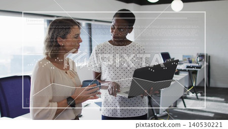 Discussing project data in open office, two coworkers in business attire holding laptop, mug, HUD Discussing project data in open office, two coworkers in business attire holding laptop, mug, HUD 140530221