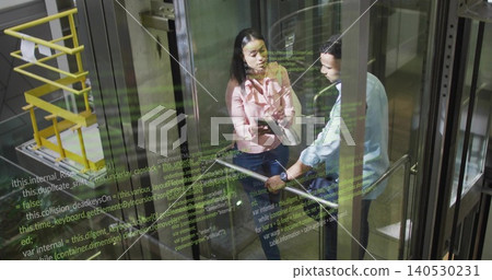 Holding tablet, pair wearing pink blouse and blue shirt talking in glass elevator with code Holding tablet, pair wearing pink blouse and blue shirt talking in glass elevator with code 140530231