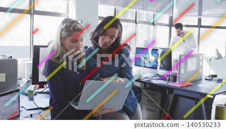 Reviewing two women leaning over laptop at open-plan office, wearing denim shirt and navy blouse Reviewing two women leaning over laptop at open-plan office, wearing denim shirt and navy blouse 140530233