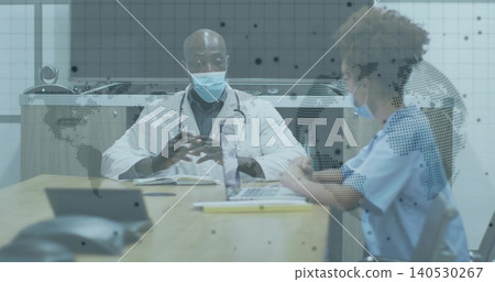 Reviewing documents doctor in lab coat, colleague in scrubs at clinic table, laptop, map partition Reviewing documents doctor in lab coat, colleague in scrubs at clinic table, laptop, map partition 140530267