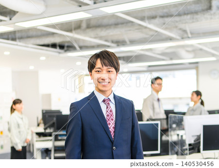 A Japanese man in a suit smiling in an office. A Japanese man in a suit smiling in an office. 140530456