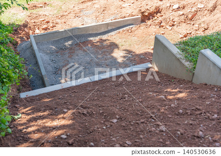 High angle overview looking down on concrete retaining blocks being aligned to create structured landscaping steps on a backyard slope. Outdoor construction site process showing hillside grading and 140530636