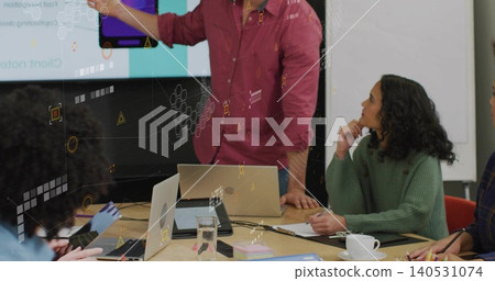 Presenting man in maroon button-down shirt gesturing at screen in meeting room, laptops visible Presenting man in maroon button-down shirt gesturing at screen in meeting room, laptops visible 140531074
