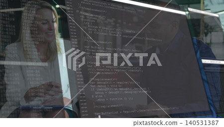 Holding notepad, colleagues in light blouse and dark blazer reviewing code on monitor in office Holding notepad, colleagues in light blouse and dark blazer reviewing code on monitor in office 140531387