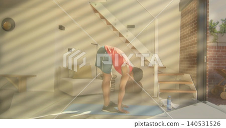 Man in red tank and dark shorts folding forward on blue mat at home, with bottle Man in red tank and dark shorts folding forward on blue mat at home, with bottle 140531526