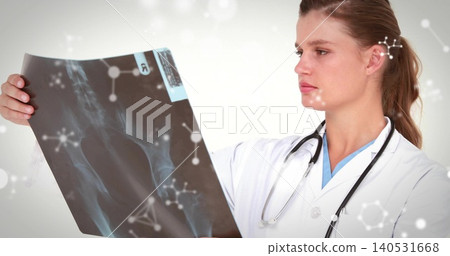 Examining clinician wearing lab coat and blue scrubs, holding pelvic X-ray, stethoscope in clinic Examining clinician wearing lab coat and blue scrubs, holding pelvic X-ray, stethoscope in clinic 140531668