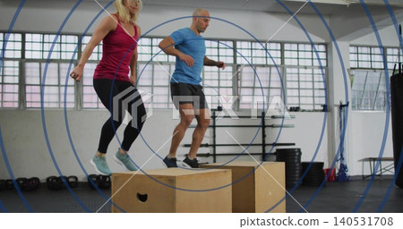 Jumping two partners landing on plyo boxes in fitness gym, wearing maroon tank and blue shirt Jumping two partners landing on plyo boxes in fitness gym, wearing maroon tank and blue shirt 140531708