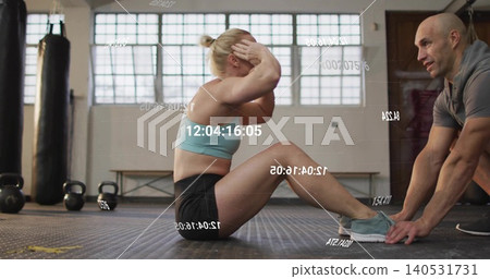 Doing sit-ups trainee wearing gear at gym, trainer holding feet with kettlebells, timestamp overlay Doing sit-ups trainee wearing gear at gym, trainer holding feet with kettlebells, timestamp overlay 140531731