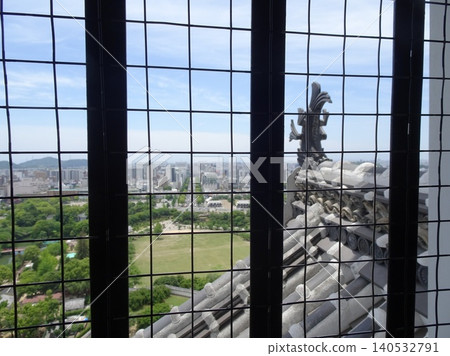 A view of the shachi (mythical fish-like creature) roof tiles and the city of Himeji as seen through the lattice windows of the main keep of Himeji Castle. A view of the shachi (mythical fish-like creature) roof tiles and the city of Himeji as seen through the lattice windows of the main keep of Himeji Castle. 140532791
