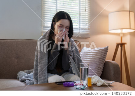Asian woman blowing nose on sofa at home for cold and flu symptoms Asian woman blowing nose on sofa at home for cold and flu symptoms 140533172