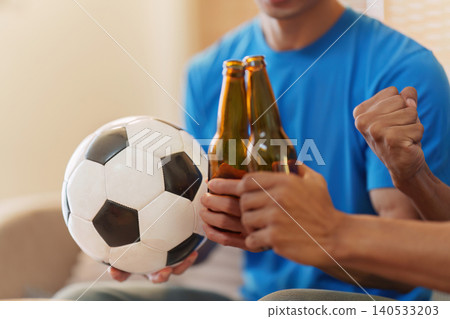 Asian men toasting beer bottles watching football game at home Asian men toasting beer bottles watching football game at home 140533203