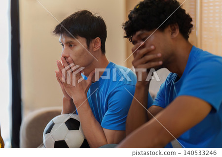 Asian men showing disappointment watching football game at home Asian men showing disappointment watching football game at home 140533246