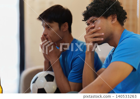 Asian men showing disappointment watching football game at home Asian men showing disappointment watching football game at home 140533263