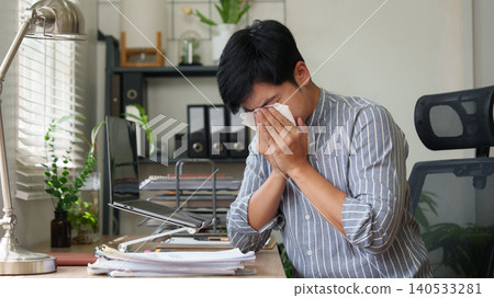 Asian man blowing nose with tissue while working from home office Asian man blowing nose with tissue while working from home office 140533281