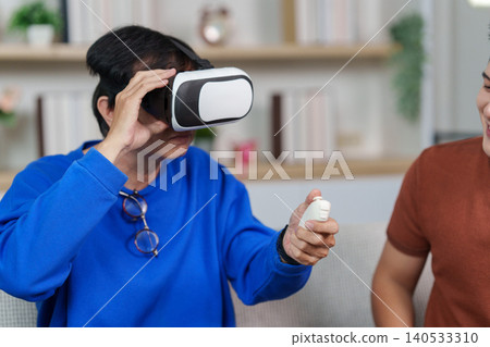 Asian senior man experiencing virtual reality gaming with young man at home Asian senior man experiencing virtual reality gaming with young man at home 140533310