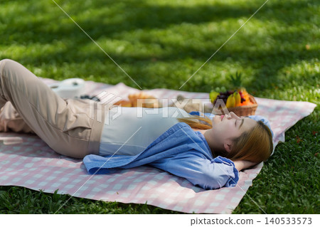 Asian woman in 20s relaxing on picnic blanket in park 140533573