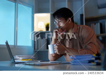 Asian man in 20s thinking while working late at home office with coffee 140533634