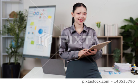 Confident Asian woman in 20s standing with clipboard at home office Confident Asian woman in 20s standing with clipboard at home office 140533790