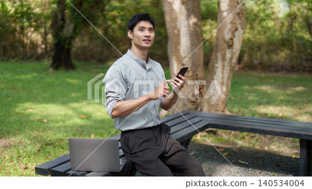 Asian man working remotely with laptop and smartphone in green park Asian man working remotely with laptop and smartphone in green park 140534004