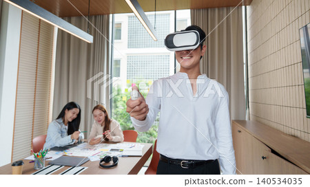 Asian man using virtual reality headset with controller in modern office. Asian man using virtual reality headset with controller in modern office. 140534035