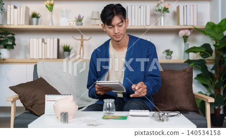 Asian man budgeting personal finance and saving money with piggy bank at home 140534158