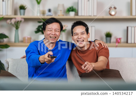 Happy Asian senior man and young man watching TV at home Happy Asian senior man and young man watching TV at home 140534217