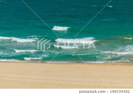 Expansive view of turquoise Mediterranean waters meeting sandy coastline, with a small pair of beachgoers enjoying peaceful summer relaxation Expansive view of turquoise Mediterranean waters meeting sandy coastline, with a small pair of beachgoers enjoying peaceful summer relaxation 140534302
